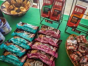 Fair Trade products, tea, coffee, chocolate and more spread across two tables with maroon tablecloths with Fair Trade members ready to help out