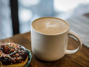 A donut with sprinkles next to a coffee mug with foam that shows a heart