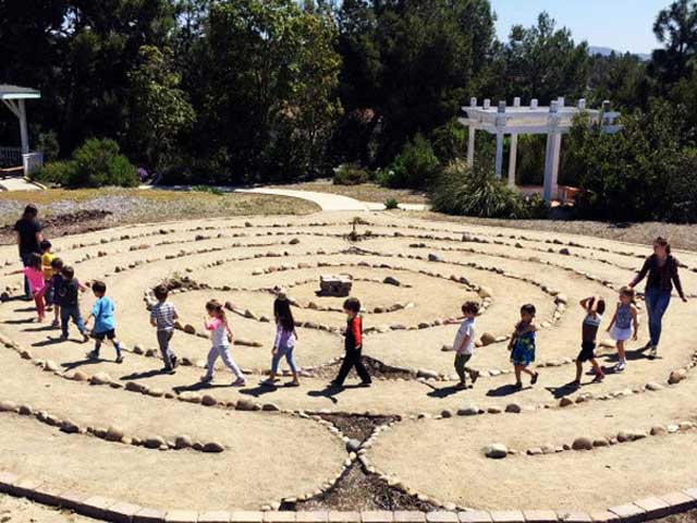 People both small and tall walking the labyrinth at Palomar Fellowship with the memorial fountain and trees in the background