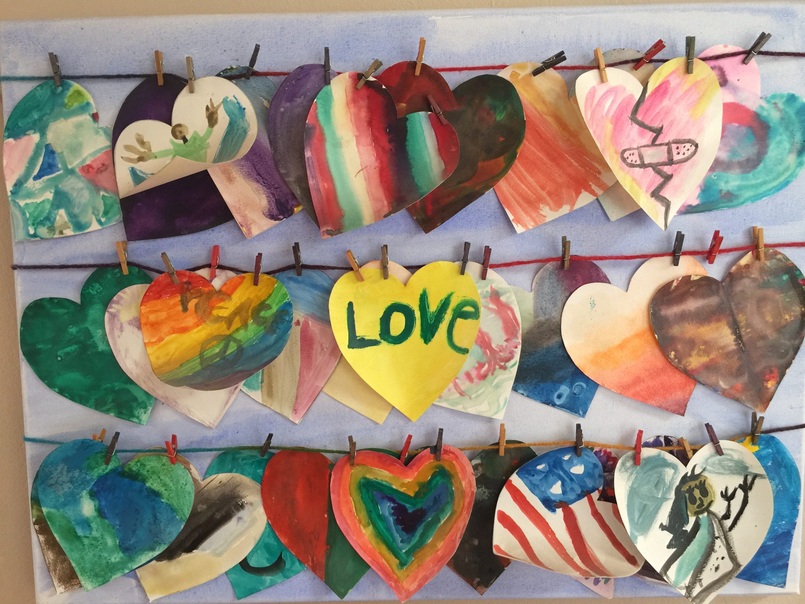 decorated paper hearts clipped to three clothes lines with the word LOVE in the middle of a center, yellow heart